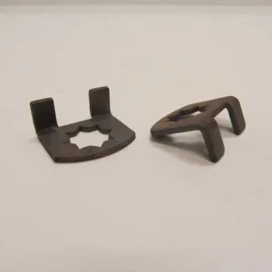 Two dark metal clips or brackets on a white surface, one flat with a central cutout and two upright prongs, the other bent into a V-shaped clip nearby.