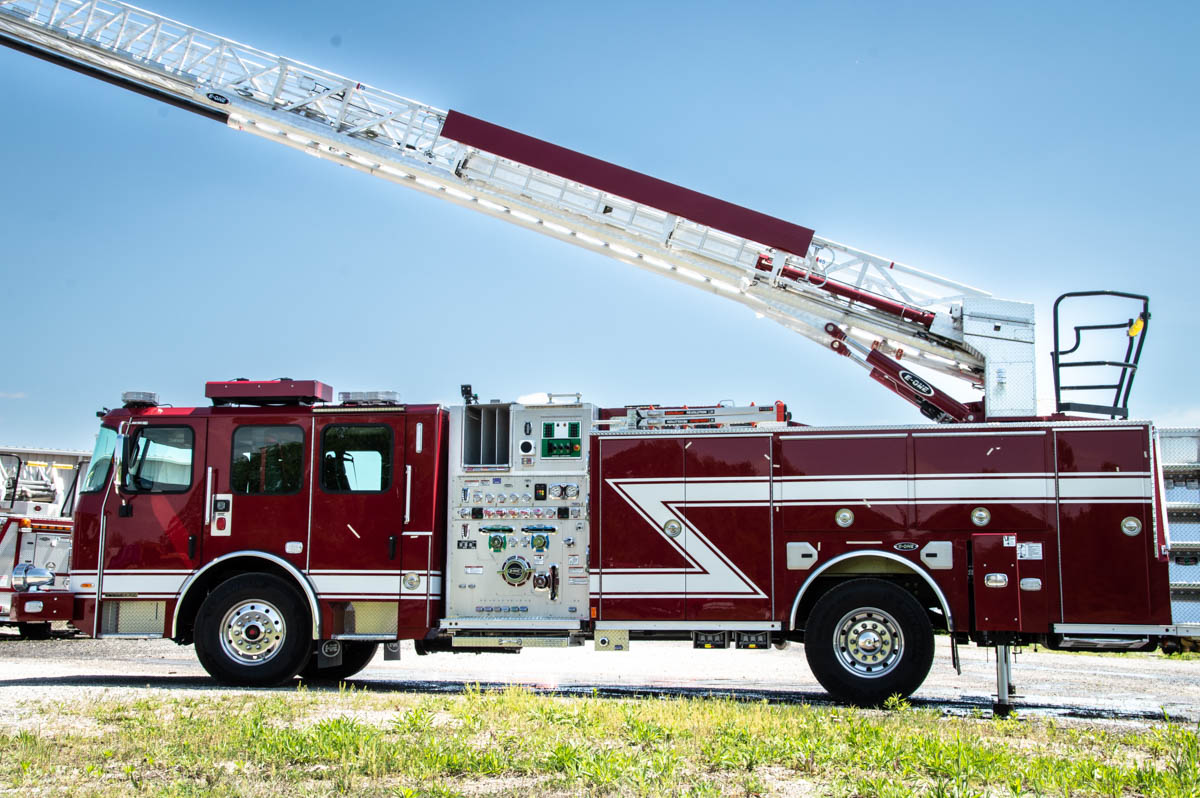 148889_aerial-6 Red fire engine with an elevated ladder parked on a gravel lot under a clear blue sky.