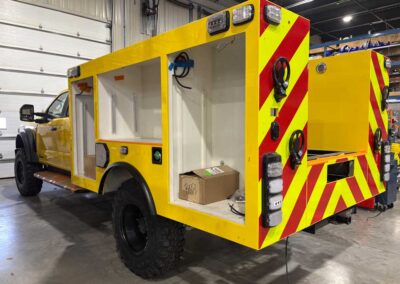 Yellow utility service truck in a workshop with open storage bays and a bright chevron-patterned rear for visibility