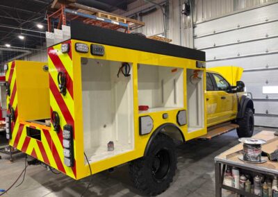 Yellow emergency utility truck in a workshop with open storage bays and chevron safety stripes on the rear.