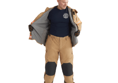 Full-body firefighter in tan turnout gear unzipping jacket to reveal navy shirt with fire department emblem on chest
