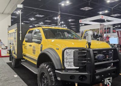 Yellow fire rescue truck on display at an indoor expo, with ladder rack and heavy front bumper.