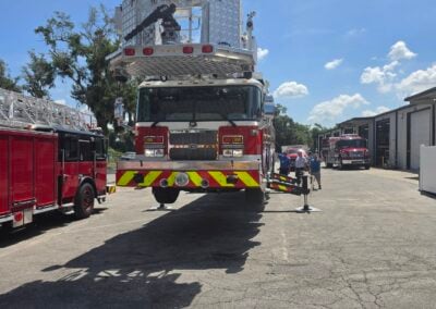 Fire truck with an elevated platform on its roof, parked in a lot as crew members walk nearby.