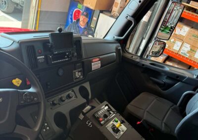 View from the truck cab showing dashboard controls, center console, and a technician outside at a service counter with boxes behind him, through the windshield.