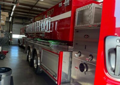 Red fire engine inside a garage with ladders secured along the side and diamond-plate compartments visible by the walk-side.