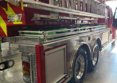 Side view of a red fire truck with a long ladder rack and multiple silver ladders secured along the side.