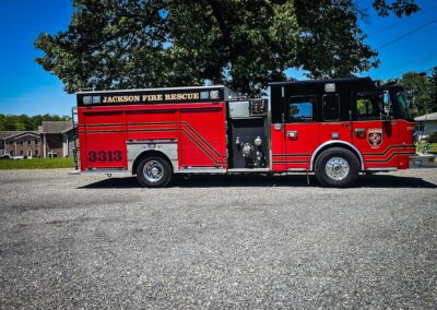 Jackson Fire Rescue fire engine parked on a gravel lot under a large tree with suburban houses in the background