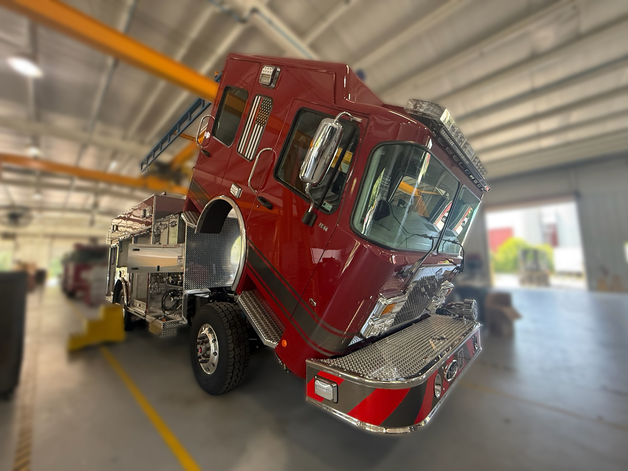 Angled view of a red fire engine inside a workshop, with metal steps and storage nearby.