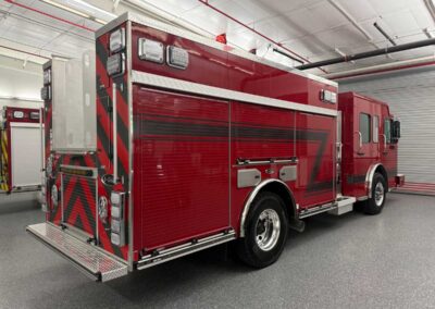 Red fire apparatus parked in a station garage, showing side compartments and rear step platform for access to equipment