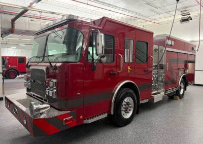 Front three-quarter view of a red fire engine inside a bright garage, chrome bumper and equipment compartments visible outside the cab.