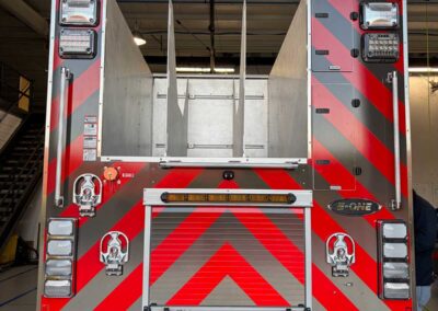 Rear view of a red fire truck with chevron red and gray stripes, emergency lights, and equipment compartments