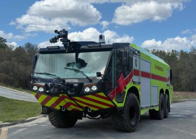 Front view of a green and yellow fire engine with a roof-mounted camera rig and chevron-patterned bumper parked on a road.