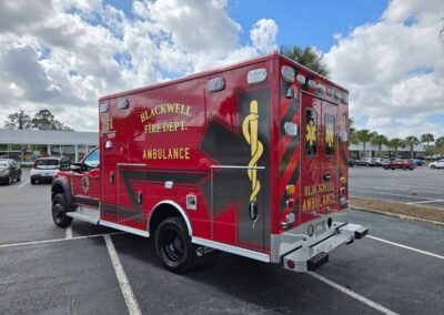 Red Blackwell Fire Department ambulance parked in a lot, side and rear views visible with gold medical symbol and department text on the sides.