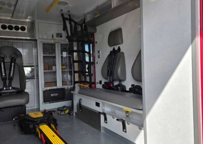 Interior of an ambulance with a lowered patient stretcher along the floor and seating along the wall.