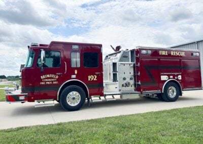 Red fire engine with 'Brimfield Community Fire Prot. Dist. 192' parked on a driveway under a cloudy sky.
