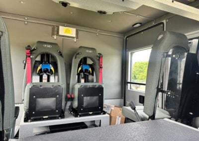 Interior of an aircraft cabin with gray helicopter seats and red seat belts, viewed from the back looking toward the cockpit area.