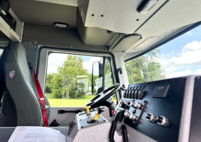 Driver's cabin of a rugged utility vehicle with a row of switches, gauges, and a coiled microphone on the console