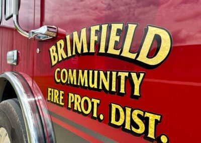 Close-up of a red fire truck side with large yellow lettering and chrome mirrors.