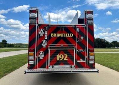 Rear view of a red-and-black chevron-pattern fire truck with 'BRIMFIELD' lettering and the number 192, parked on a sunny day.