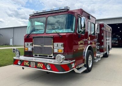 Red fire engine parked outside a fire station, front view with chrome grille and bumper lights