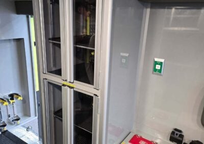 Tall glass-fronted storage cabinet in an ambulance, with yellow 'Max loaded capacity' stickers on each door.