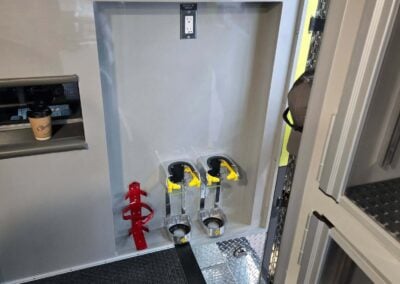 Maintenance cabinet interior with three yellow-levered controls and a red strap at the lower left; metal floor plate and an electrical outlet above.