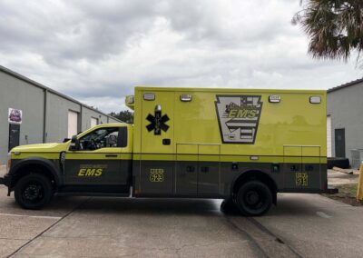 Bright yellow EMS ambulance parked outside a gray industrial building; Bryan County EMS logo visible on the side.