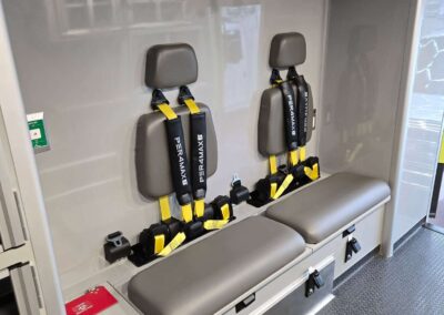 Wall-mounted emergency rescue gear with gray seats and yellow straps inside a clinical van or cabin, ready for use in evacuations or training