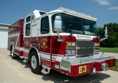 Front three-quarter view of a red and white Hannibal Fire Department fire engine parked on a driveway, with chrome bumper and emergency lights visible.