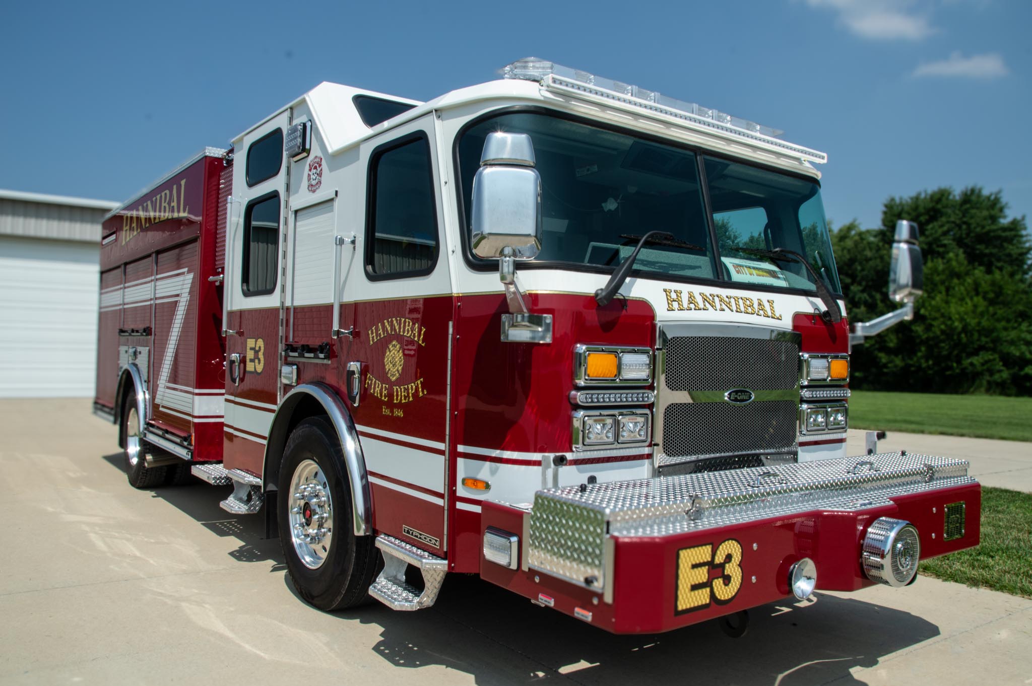 Front and side view of a red Hannibal Fire Department fire engine parked outdoors on a sunny day.