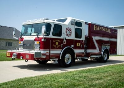 Front and side view of a red and white Hannibal fire engine parked on a suburban street, with fire department emblem on the door and 'Hannibal' lettering