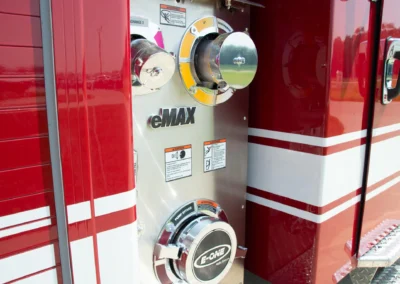 Close-up of a fire truck pump panel with gauges and chrome fittings on a red exterior piece of the truck.