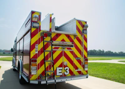 Rear view of a fire engine with bright red and yellow chevrons, ladders, and equipment bays on a sunny day.