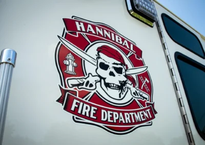 Close-up of a fire department emblem on a white truck door, featuring a skull with crossed swords and red banner text Reading 'FIRE DEPARTMENT' (informational image).