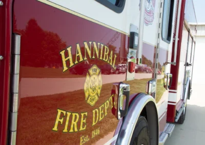 Side view of a red Hannibal Fire Department fire truck with a crest emblem and gold stripe along the door