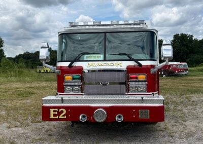 Front view of a red fire engine with a chrome grille, emergency lights, and 'MACON' on the bumper; clear windshield and reflective mirrors.