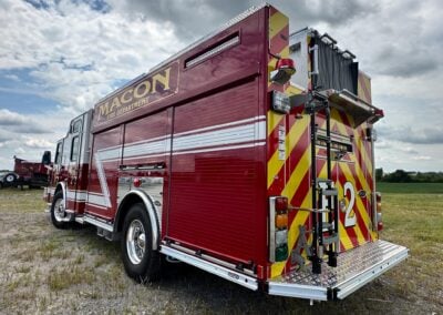 Rear and side view of a red Macon Fire Department fire engine with yellow chevrons parked on a grassy field, showing ladders and equipment.