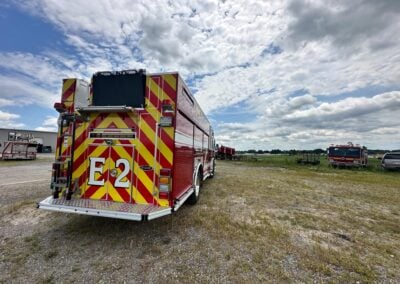 Rear view of a red fire engine with yellow-and-red chevron markings on a gravel lot under a cloudy sky.