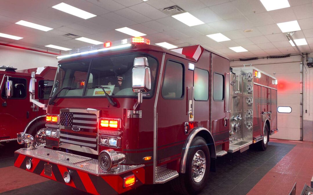 Red fire engine inside a garage with flashing emergency lights on the roof and chrome detailing on the bumper.
