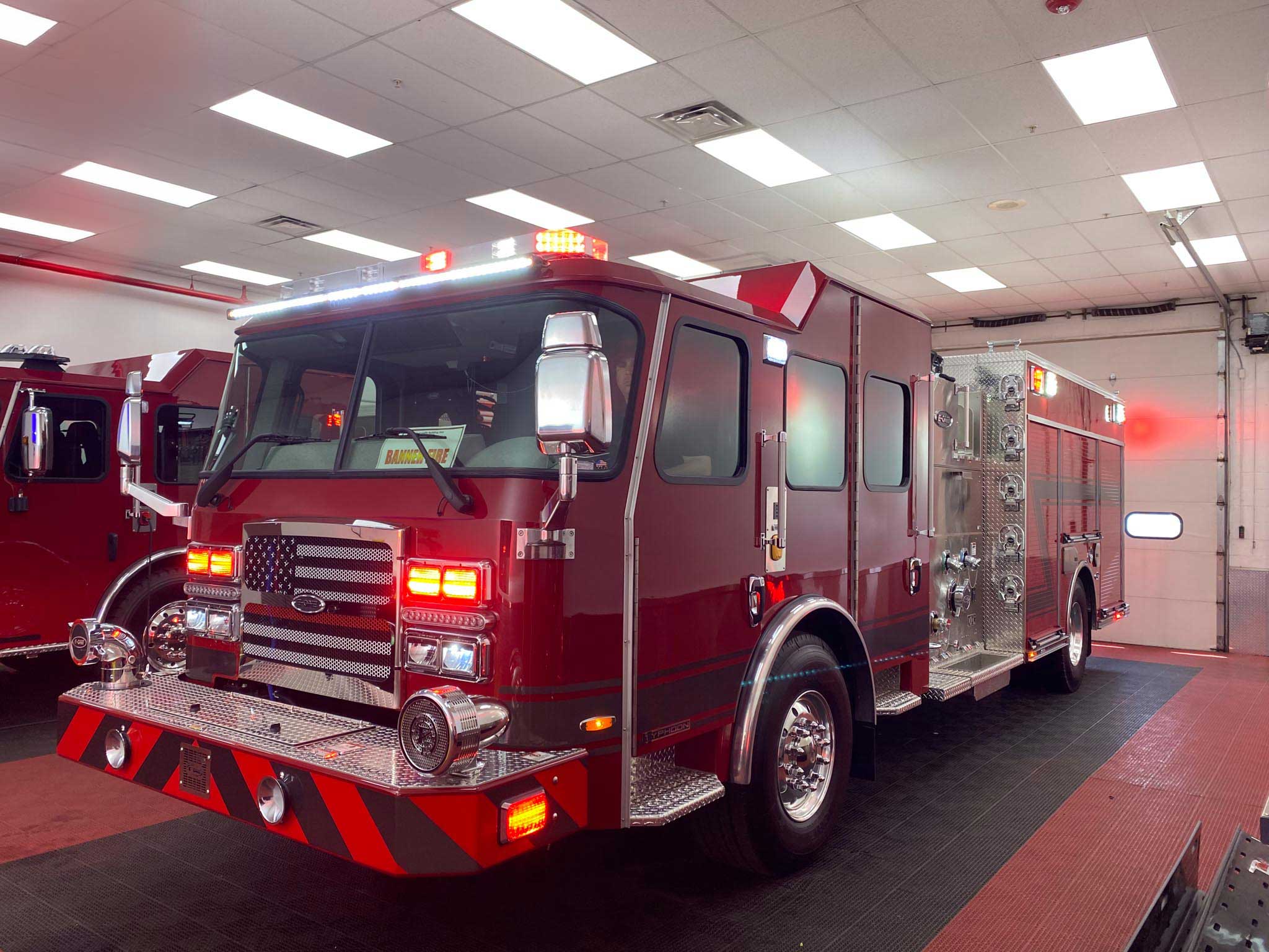 Red fire engine inside a garage with flashing emergency lights on the roof and chrome detailing on the bumper.