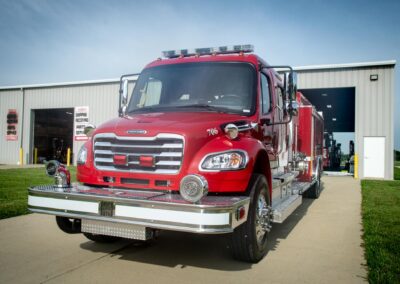 Large red fire truck parked in front of a fire station with chrome bumper and equipment compartments visible.