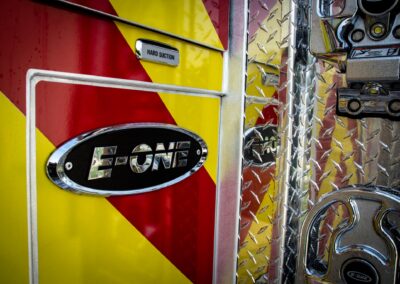 Close-up of a fire truck side with red and yellow diagonal panels, chrome 'Hard Suction' badge, and diamond-plate metal.