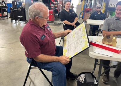 Older man in a maroon shirt reads a laminated menu at a table in a fire station, with a red fire truck in the background.