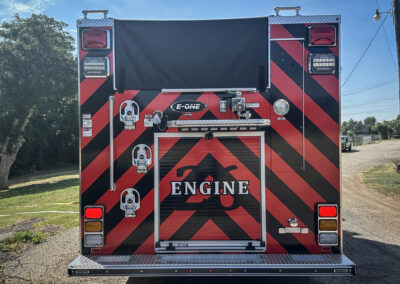 Rear view of a red and black chevron-pattern fire engine with equipment panels and lights visible on both sides, and the word ENGINE partially showing at the bottom.