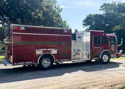 Red fire engine parked outdoors with trees in the background, showing 'KINGFISHER' on the side panel.