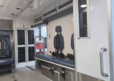 Interior of an ambulance with blue cushioned seats, cabinets, and equipment along the wall; metal floor and ceiling panels visible