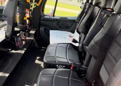 Rear cabin of a black-leather passenger van with mounted rescue equipment and a yellow grab handle by the window.