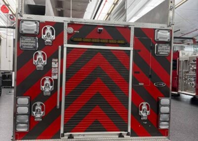 Rear of a red fire truck with diagonal chevron stripes and multiple compartments inside a fire station.
