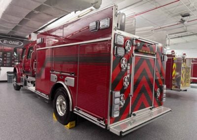 Red fire engine parked indoors, showing rear compartments, ladders, and chevron markings on the back.