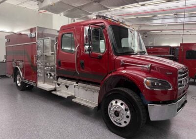 Red fire engine parked indoors, showcasing diamond-plate compartments and chrome detailing along the side.